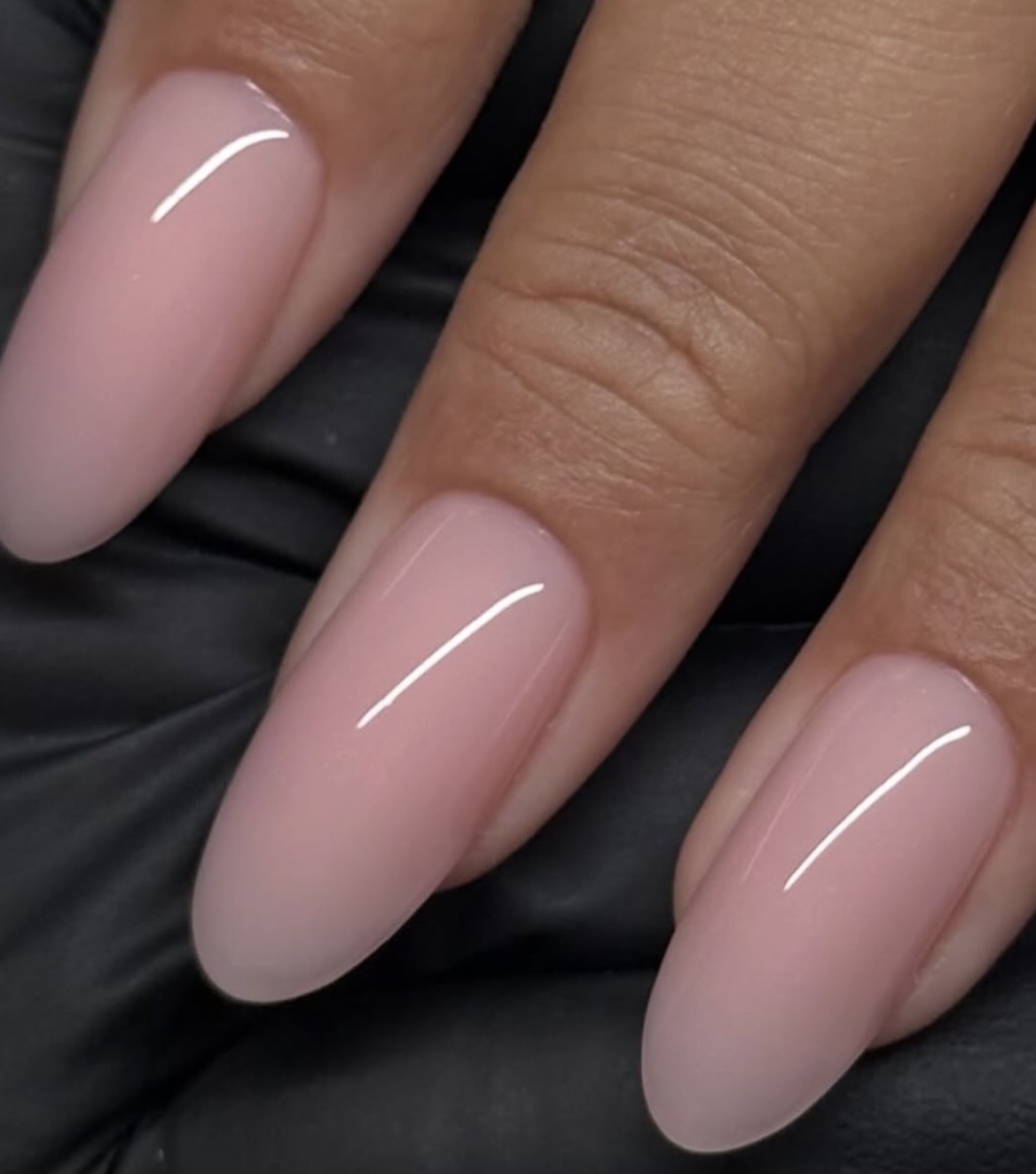 Lange amandelnagels in een glanzend nude roze, gezet bij Maison Delux