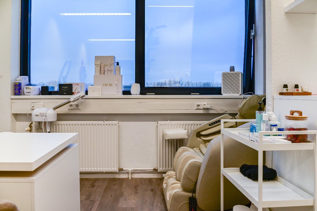 Raamzijde van de studio met massagestoel, verzorgingskarretje en producten op de vensterbank